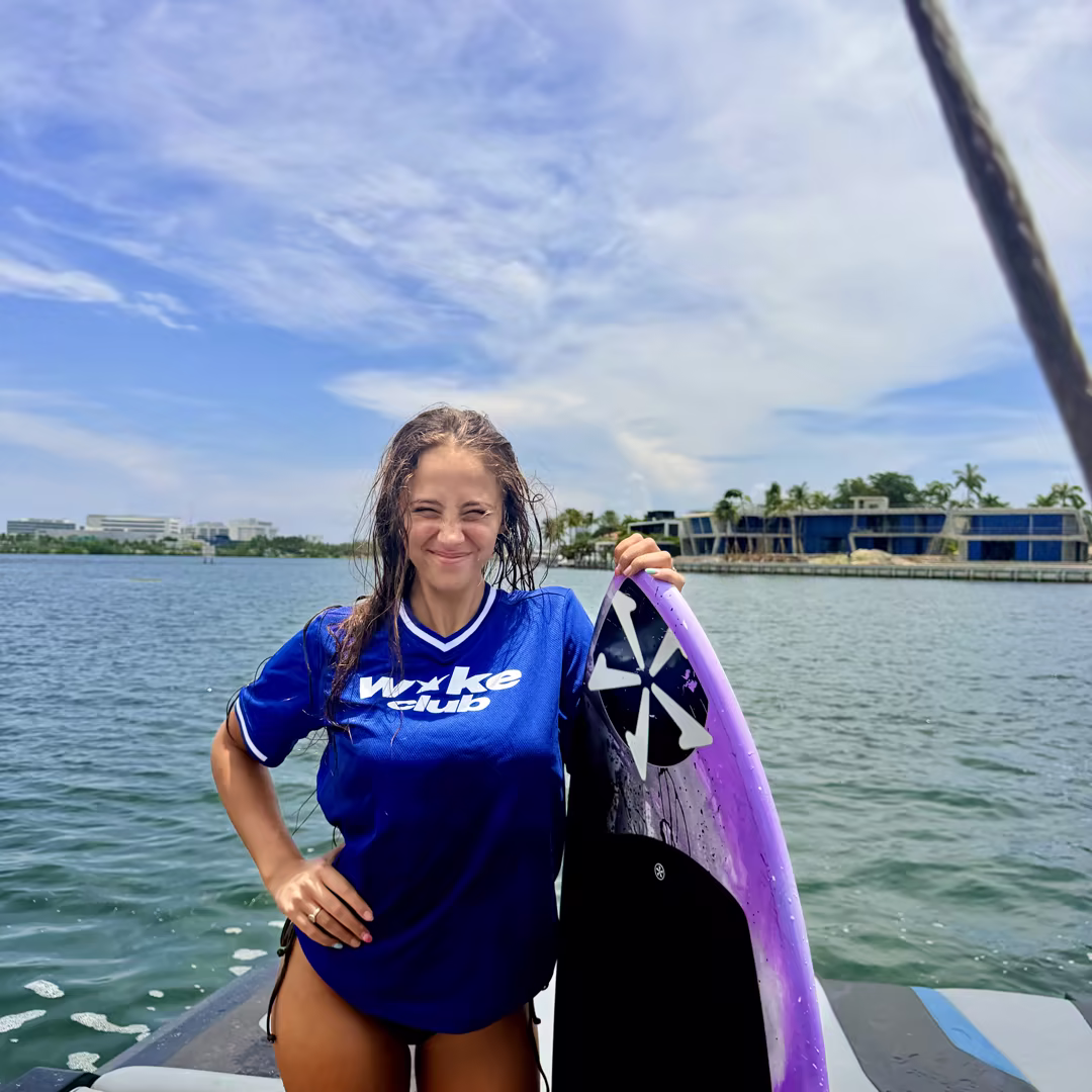 A guest in a Wake Club jersey holding her wakesurf board on Biscayne Bay
