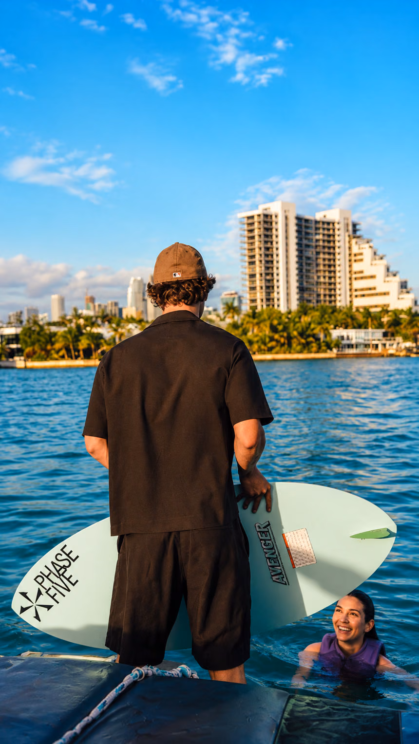A guest on the boat with a wakesurf board, a friend smiling in the water and the Miami skyline behind — the kind of day you can gift