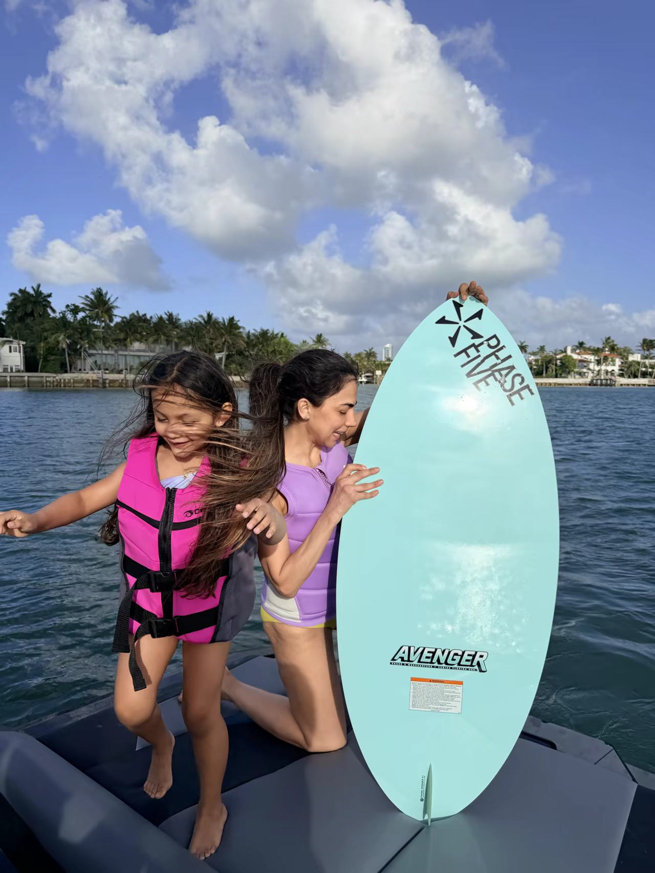 Dos niñas con chalecos salvavidas bien ajustados en el barco, listas para montar, sosteniendo una tabla de wakesurf